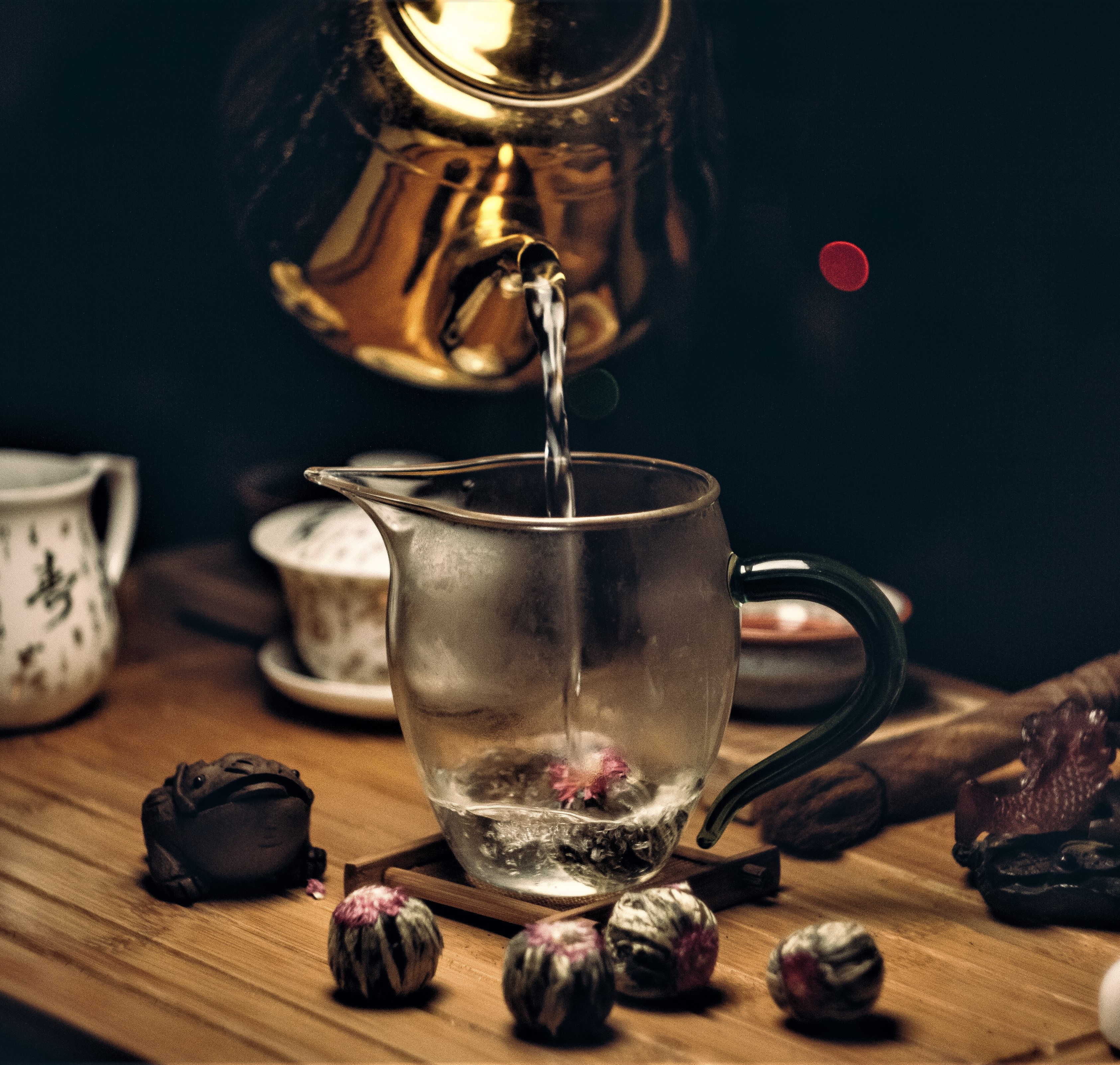 a teapot pouring water into a blossoming tea ball in a cup